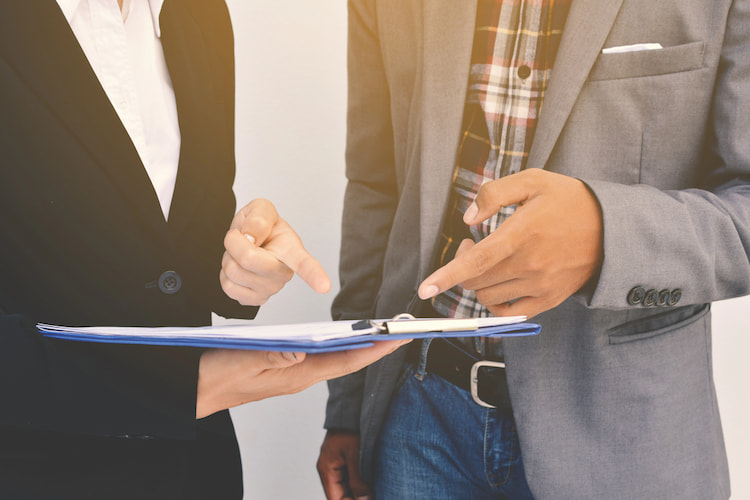 Two individuals pointing down at their work in order to collaborate well. 